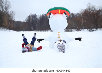 Boy lies near upside down snowman with snowtube at winter day