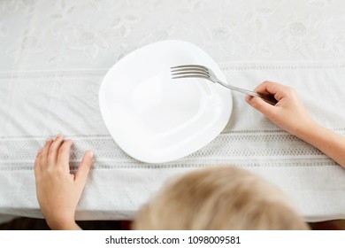 Boy Is Looking At An Empty Plate With A Fork In His Hand, A Hungry Child At The Table