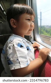 A boy is looking out of the train window during the daytime