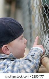 boy looking through a chain link fence and pointing at something of interest