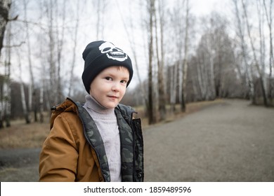 A Boy Looks At The Camera With A Sly Look, Outdoors In Winter Clothes, A Black Hat And A Mustard Jacket, A Small Handsome Man