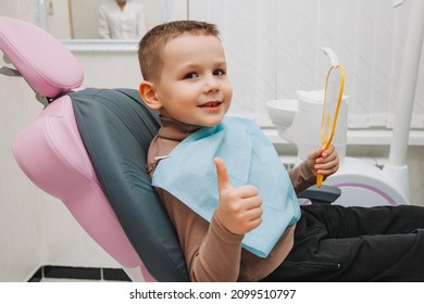 boy looks in the mirror with a toothy smile, sitting on a chair with a dentist in the dental office. - Shutterstock ID 2099510797