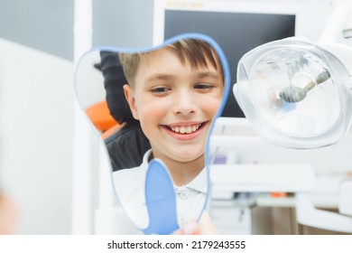 boy looks in the mirror with a toothy smile, sitting on a chair with a dentist in the dental office. - Powered by Shutterstock