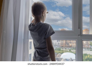 Boy looks out window at city, dreaming of future. Self-knowledge in pre-adolescence. - Powered by Shutterstock