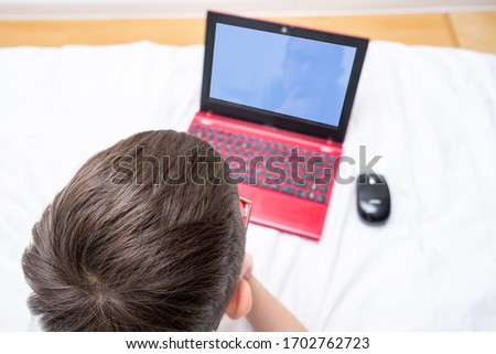 A boy lying in bed with a laptop,distance and e-learning during quarantine and self isolation, online digital education, top view.