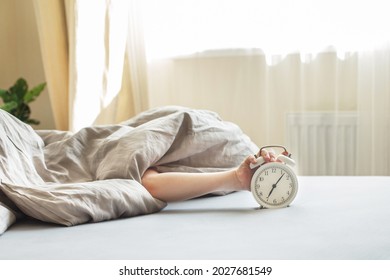 boy lying on the bed under a blanket and stopping alarm clock in the morning. childs hand reaching for the alarm clock to turn it off.