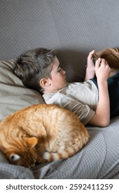 Boy lying on couch using smartphone next to a sleeping cat