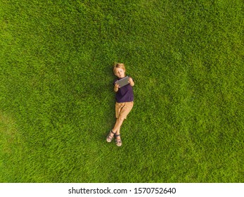 Boy lying on the grass in the park and looks at the tablet. Photos from the drone, quadracopter - Powered by Shutterstock