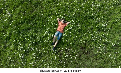 Boy lying on the green grass from above. Top view. Teen in sunasses. Teen looking in camera