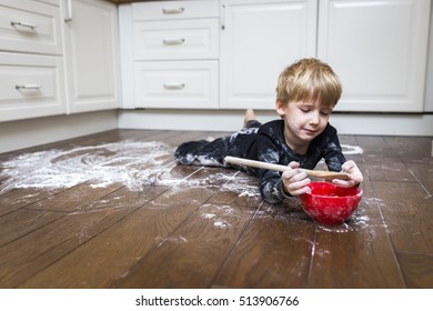 A boy lying on the kitchen floor and playing with flour. 
