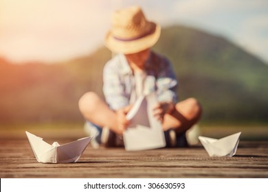 Boy Make A Paper Boat Sitting On The Wooden Pier