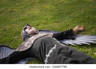 Boy In Make Up With White Face And Black Eyes, Dressed As An Angel Of Death With Wings, Lying On His Back On The Grass With A Lost Look. Concept Halloween, Autumn, Trick Or Treat, Fear, Terror.