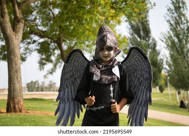 Boy In Make Up With White Face And Black Eyes, Dressed As An Angel Of Death With Wings And Haunting Look Celebrating Halloween In An Outdoor Park. Autumn Concept, Trick Or Treat, Fear, Terror.