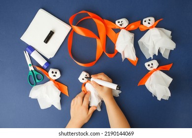 Boy Makes Halloween Toys Ghost From White Paper Napkin. Creative DIY For Kids On Classic Blue Background. Home Decor Project Party. Halloween Crafts Inspiration, Recycle Concept