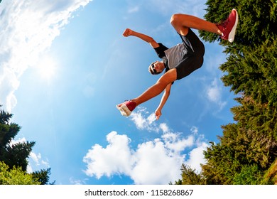 Boy Makes A Jump In A Mountain Meadow. View From Below. Daylight, Summer Season, Fisheye Lens.