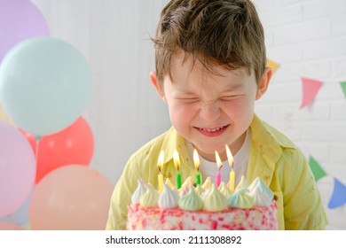 a boy makes a wish in front of a birthday cake with candles. Funny facial expression, emotions, closed eyes, desire thinks. Horizontal photo.