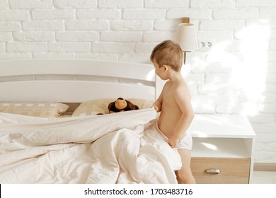 Boy Making Covering Bed And Teddy Bear Blanket. Preschooler Child Play In Childhood Game And Put Sleep Toy In Bed. Caucasian Kid, Scone Lamp On White Brick Wall On Background. Bedroom Stylish Interior