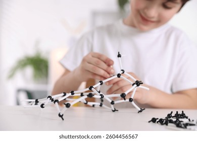 Boy making DNA structure model at desk indoors, closeup. Space for text