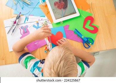 Boy making greeting card according to the picture on the digital tablet, view from the top