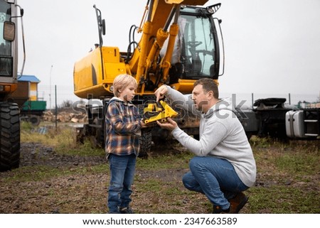 boy and man on background of construction equipment - excavators are enthusiastically examining toy bulldozer. Spend the day with your son. The boy's interest in machines and their work. Father's Day