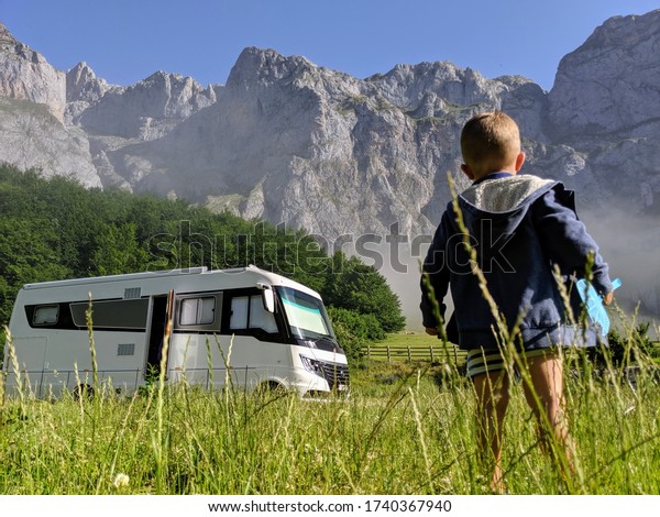 Boy in meadow with camping car\
overlooking the glacial circus of Fuente Dé in Picos de\
Europa