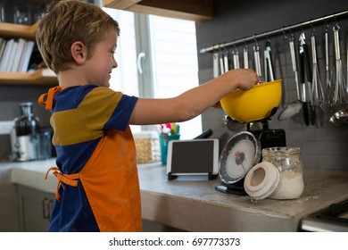 Boy measuring food in yellow bowl over kitchen scale at counter