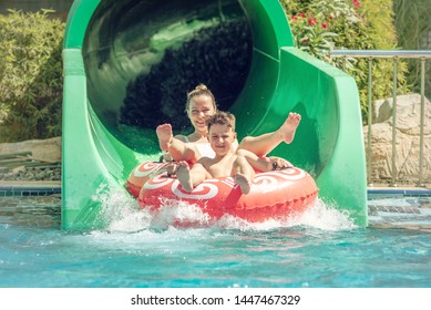 Boy With Mom On Floater Sliding Down Slide In Waterpark.