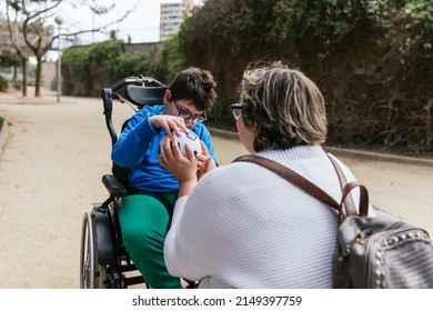 Boy With Multiple Disabilities Playing With A Soccer Ball With His Mother Outdoors In The Park.