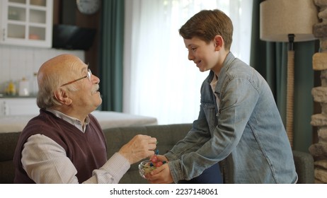 Boy offering candy in bowl to his old grandfather. Little boy offering candy to his elderly grandfather to celebrate the traditional Eid al-Fitr (candy feast) after the end of Ramadan.