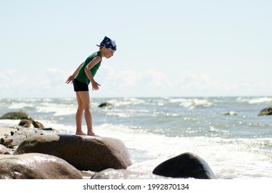 Boy On The Beach Standing On The Rock. Real Sea Background. Hot Summer Activities For Children. Holiday Theme. Active Vacation.