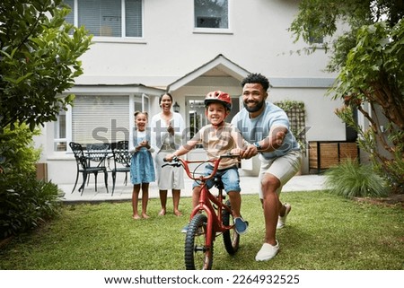 Boy on bicycle learning with proud dad and happy family in their home garden outdoors. Smiling father teaching fun skill, helping and supporting his excited young son to ride, cycle and pedal a bike