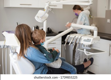 The boy on his mother's lap sitting on the dental chair, Due the Covid-19 pandemic they have face masks.