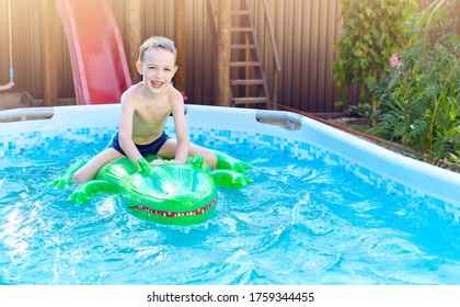 Boy On Inflatable Crocodile Float In Outdoor Swimming Pool At Home. Summer Vacation With Kids. Swim Aids And Wear For Children. Water Toys. Little Child Floating On Colorful Raft.