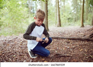 Boy On Outdoor Camping Trip In Forest Learning How To Make Fire By Rubbing Sticks Together