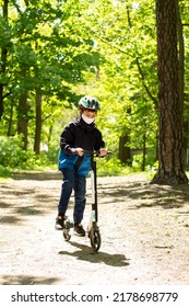 A Boy On A Scooter In A Helmet And A Medical Mask