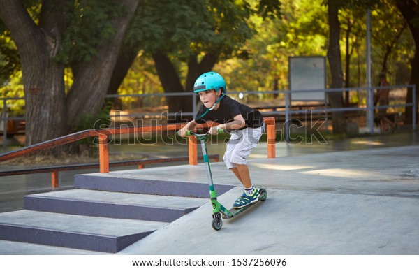 A boy on a scooter and in protective\
helmet do incredible stunts in skate park. Extreme jump. The\
concept of a healthy lifestyle and sports\
leisure