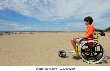 boy with orange t-shirt sitting on the special wheelchair with aluminum alloy wheels to move on the beach - Powered by Shutterstock