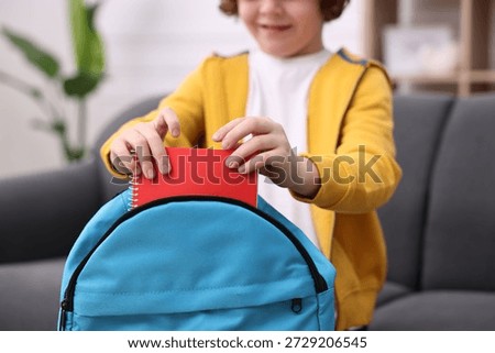 Boy packing his backpack for school on sofa at home, closeup