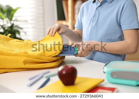Boy packing his backpack for school at desk indoors, closeup