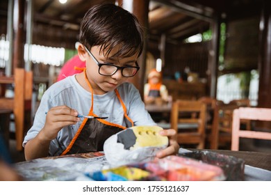 Boy painting crafts with colors in the pottery gallery along with friends - Powered by Shutterstock