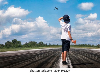 A Boy With A Paper Airplane On The Runway Looking At The Sky, Where A Real Plane Is Flying