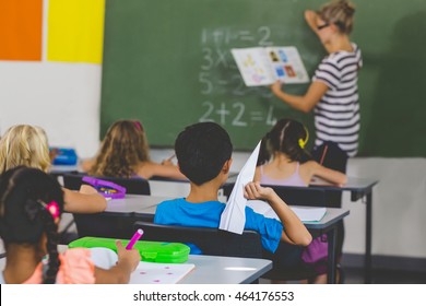 Boy with a paper plane while teacher teaching in classroom at school - Powered by Shutterstock