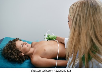 Boy Patient Getting Monitor Heart Health Using Electrocardiogram Equipment With Woman Cardiologist. Cardiogram Test For Child