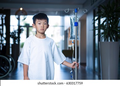 Boy patient holding intravenous iv drip stand in corridor at hospital - Powered by Shutterstock