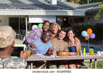 Boy Photographing Male Soldier With Family And Friends At Homecoming Party