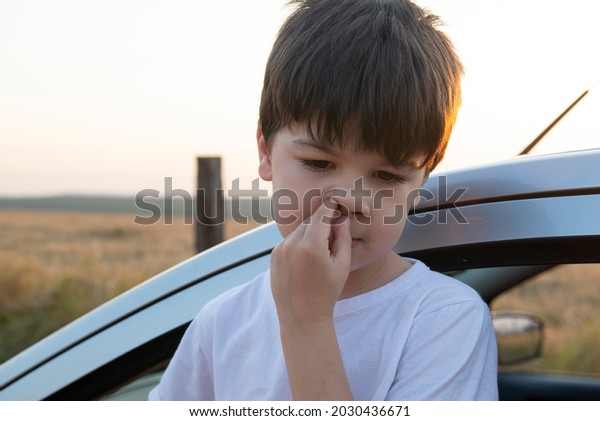 Boy picking his\
nose next to a car at sunset. Dry and hot weather brings malaise\
and respiratory problems.