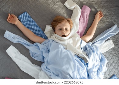 A Boy In A Pile Of Clothes On A Bed. Top View. Recycling Of Clothes. Ecological And Sustainable Lifestyle. High Quality Photo