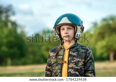 A boy in a pilot's helmet on a background of greenery. Dream concept, choice of profession, game. Copy space