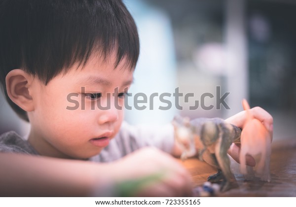 A boy play fight\
between his toys on the wood table, there are dinosaurs, whale,\
sharks and human.