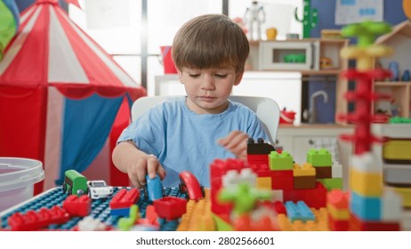 Boy playing with blocks at a table, hands touching colorful bricks and a toy car near a red tent in a building; imaginative curiosity.
